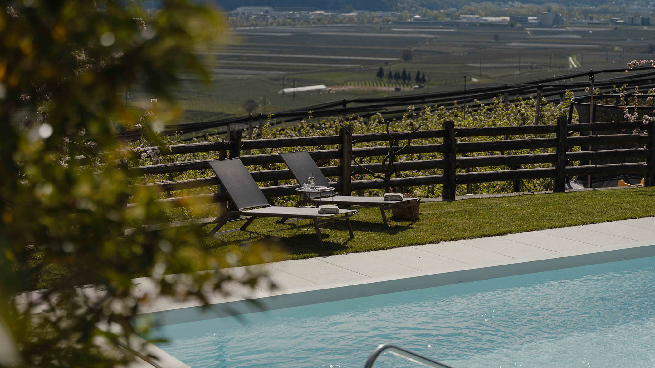 Zwei Liegestühle und ein Tisch am Pool, mit Blick auf die Weinberge und Felder in der Ferne. - Bucherhof