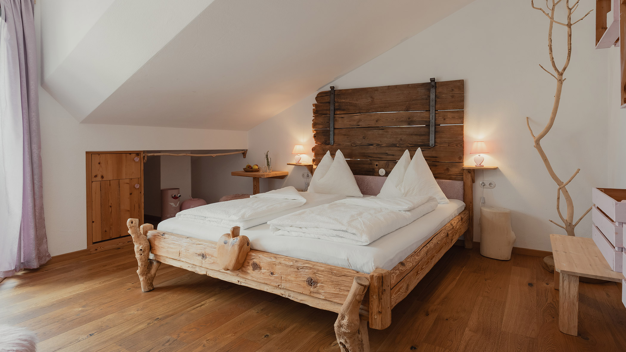 Gemütliches Schlafzimmer mit einem rustikalen Holzbett, zwei weißen Kissen, Holzboden und sanftem Tageslicht. - Bucherhof