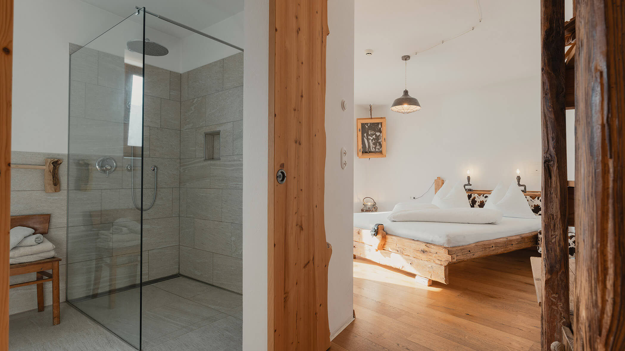 Ein modernes Badezimmer mit Glasduschkabine neben einem rustikalen Schlafzimmer mit Holzböden und einem gemütlichen Bett. - Bucherhof