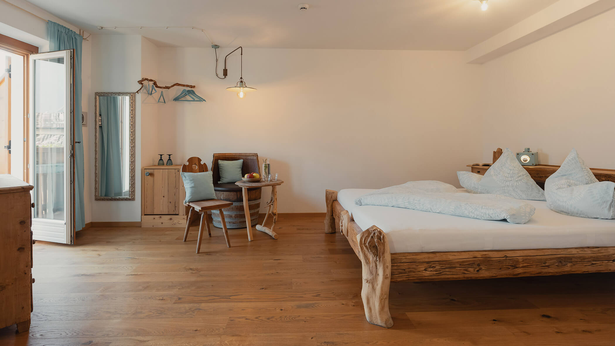 Gemütliches Schlafzimmer mit einem Holzbett, einem Tisch und Stühlen, einer offenen Balkontür und hellblauen Akzenten. - Bucherhof